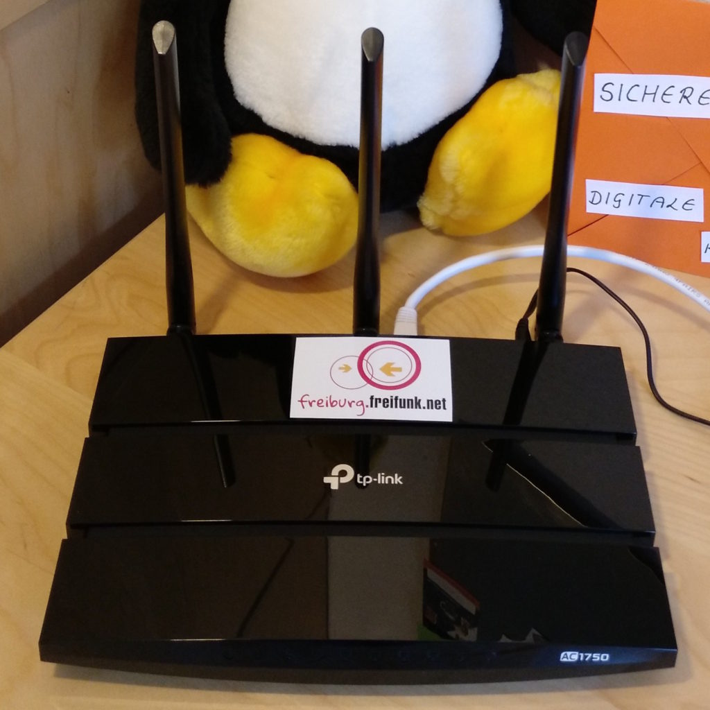 Ein zum Freifunkknoten umfunktionierter, herkömmlicher WLAN-Router des Typs Archer C7 des Herstellers TP-Link. Auf dem Gehäuse klebt oben in der hinteren Mitte ein Aufkleber mit der Aufschrift „freiburg.freifunk.net.“